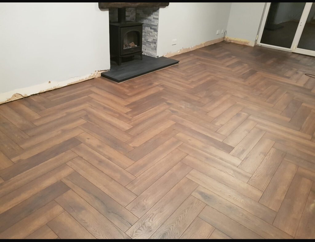 Herringbone oak laminate fitted around a fireplace hearth by Prime Carpets & Flooring